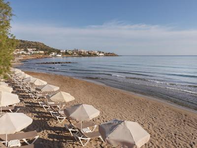 Ein ruhiger Sandstrand mit weißen Sonnenschirmen und Liegestühlen entlang der Küste.