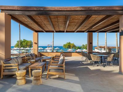 Offener Lounge-Bereich mit Holzmöbeln und Blick auf das Meer bei klarem Himmel.