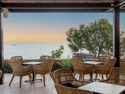 Offener Hotelbereich mit Korbstühlen und Tischen mit Blick auf das Meer und den Sonnenuntergang.