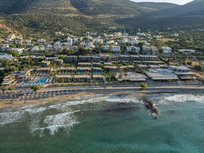 Strandhotelanlage mit Pools, Liegestühlen und Bergen im Hintergrund an der Küste.