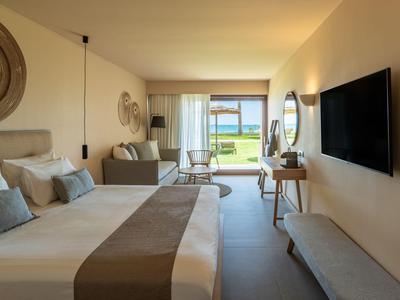 Geräumiges Hotelzimmer mit Doppelbett, Sitzbereich und Blick auf den Garten und Pool.