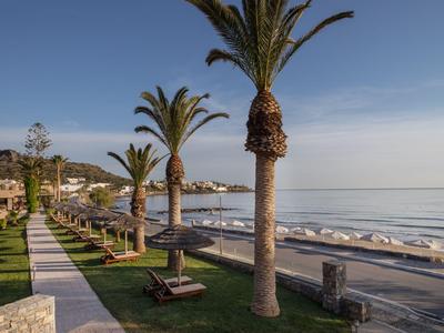 Promenade mit Palmen und Liegestühlen entlang eines ruhigen Strandes bei klarem Himmel.