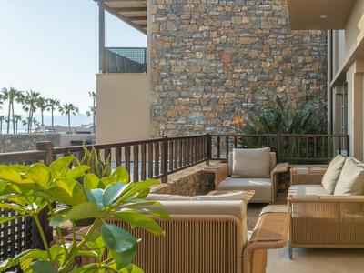 Moderne Hotelterrasse mit gepolsterten Stühlen, Steinwand und grünen Pflanzen bei Tageslicht.
