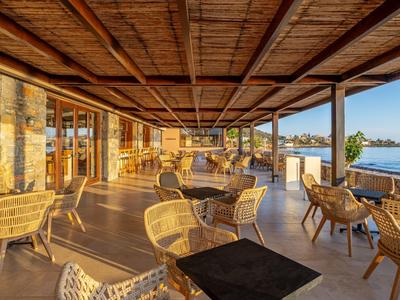 Offene Terrasse mit Rattanmöbeln und Meerblick in einem Hotel bei Sonnenuntergang.