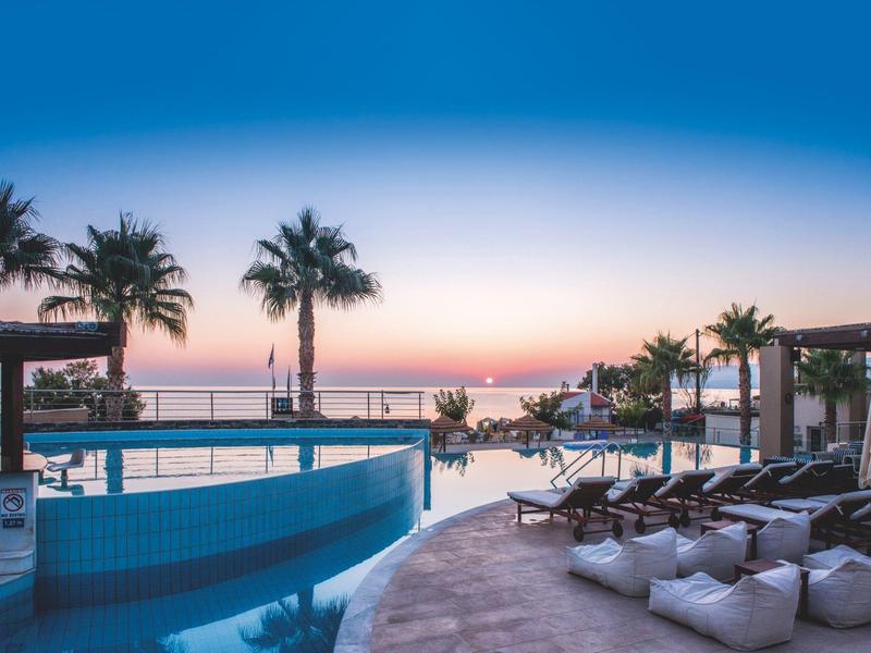Zone de piscine de la station avec palmiers et transats au coucher du soleil au bord de la mer.