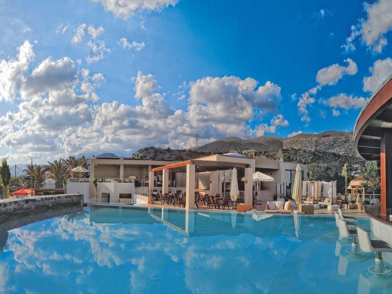 Station ensoleillé avec grande piscine, chaises longues et parasols sous un ciel bleu avec des nuages.