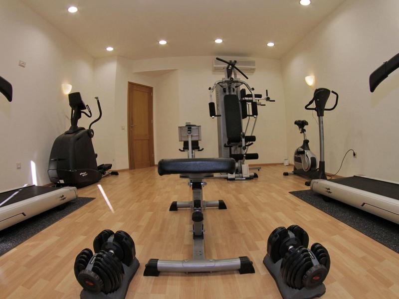 Salle de sport avec appareils d'exercice, haltères et sol en bois sous un éclairage lumineux.