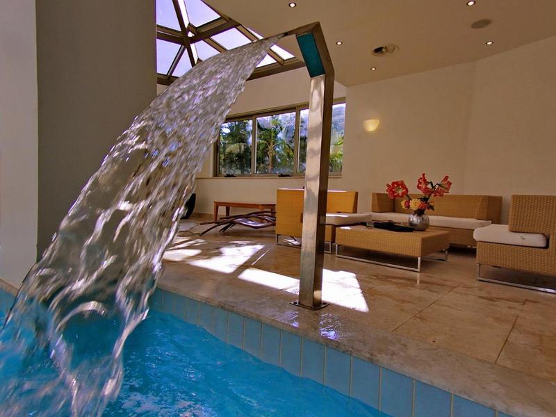 Piscine intérieure avec eau coulante d'une fontaine, sièges lounge et lumière naturelle par les puits de lumière.