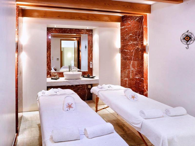 Salle de spa avec deux tables de massage, éclairage chaud, serviettes blanches et grand miroir au-dessus d'un lavabo.