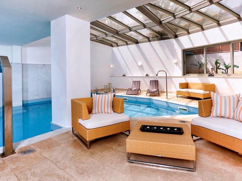 Piscine intérieure avec canapés modernes et lumière naturelle par des fenêtres de toit.