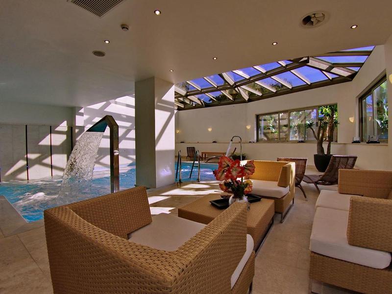 Coin salon confortable avec canapés en osier et serviettes près d'une piscine intérieure sous un plafond en verrière.