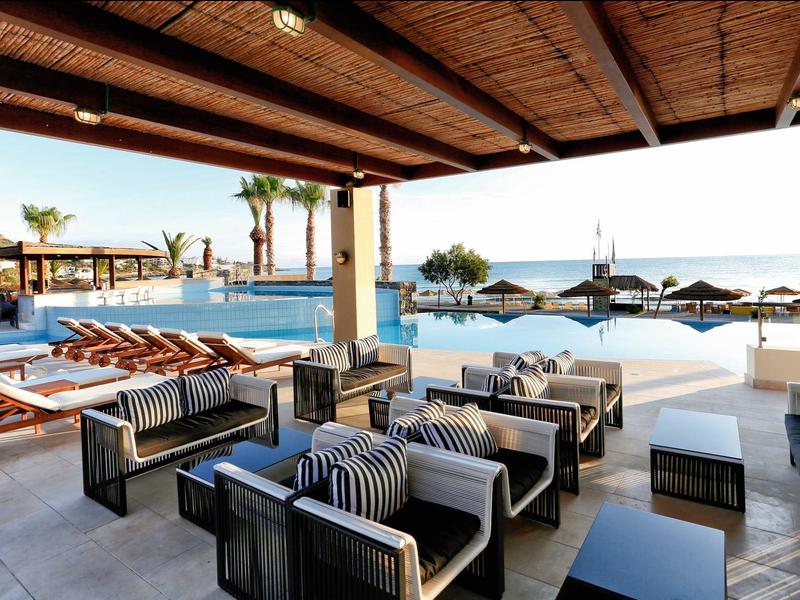 Espace lounge extérieur avec sièges et transats donnant sur une piscine et la mer.