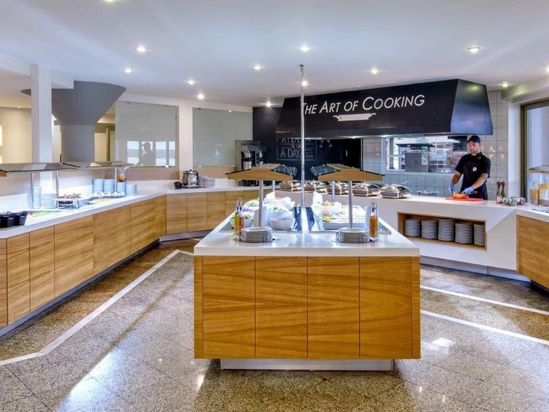 Cuisine d'hôtel moderne avec armoires en bois, stations de cuisson et grandes fenêtres, bien éclairée et spacieuse.