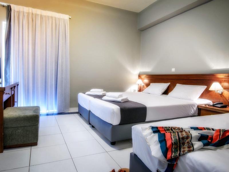 Chambre d'hôtel lumineuse avec deux lits, lampes de chevet et télévision près de la porte du balcon.