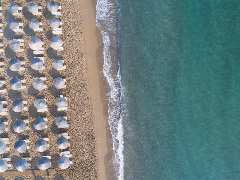 Vue aérienne de parasols en rangées sur une plage de sable près de la mer turquoise claire.