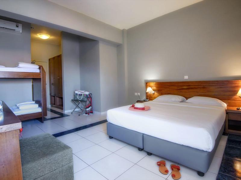 Chambre d'hôtel avec lit double, tête de lit en bois, sol carrelé et porte-bagages près de l'entrée.