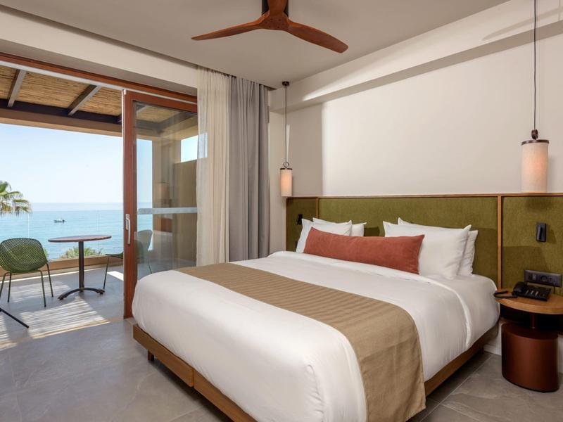 Chambre d'hôtel moderne avec lit king-size, tête de lit verte et balcon vue mer.