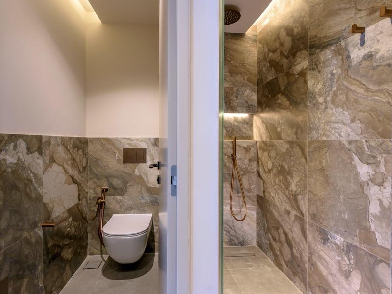 Salle de bains moderne avec toilettes et douche à l'italienne en pierre séparées par une cloison.