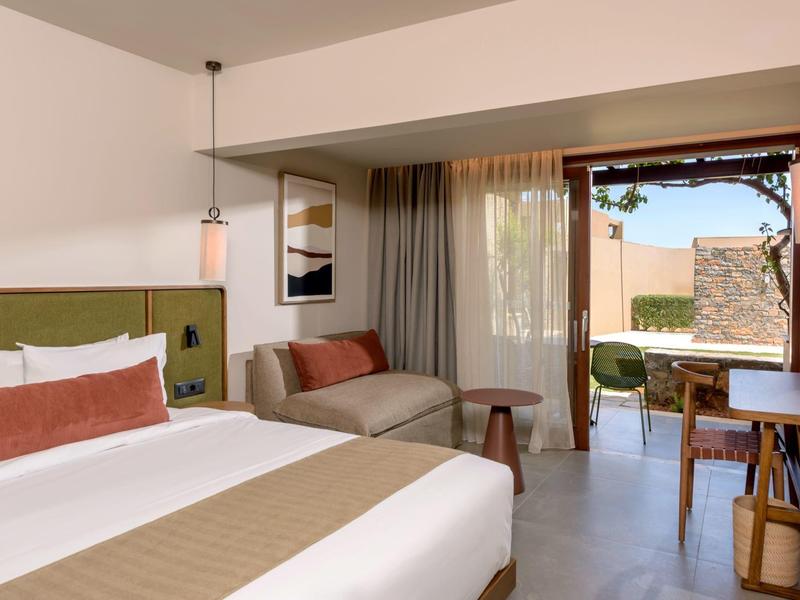 Chambre d'hôtel moderne avec lit, coin salon et balcon donnant sur le jardin