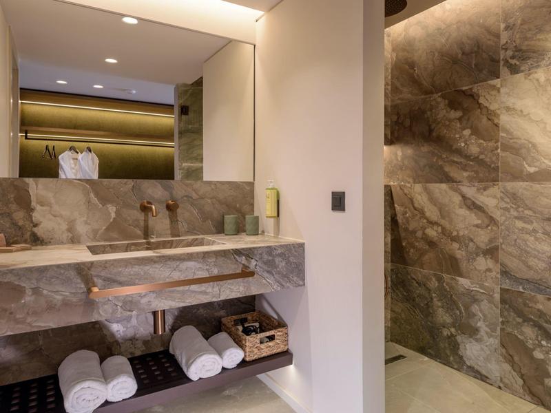 Salle de bain moderne avec lavabo en pierre, grand miroir et douche à l'italienne aux murs en pierre.