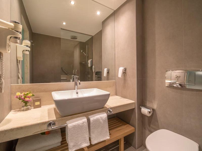 Salle de bain moderne avec lavabo, miroir, serviettes et porte-papier toilette.