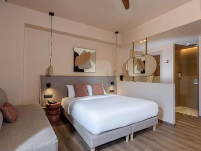 Chambre d'hôtel moderne avec lit double, canapé, miroir et décoration murale abstraite.