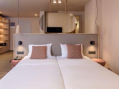 Chambre d'hôtel moderne avec deux lits simples, draps blancs et éclairage chaud.