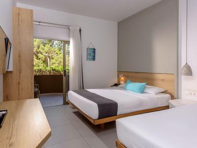 Chambre d'hôtel moderne avec deux lits, mobilier en bois et balcon avec vue sur la verdure.