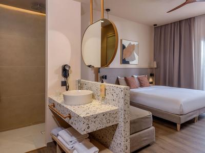 Chambre d'hôtel moderne avec lit double, lavabo en marbre et grande fenêtre avec rideau.