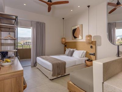 Chambre d'hôtel moderne avec lit double, meubles en bois et balcon en pleine journée.