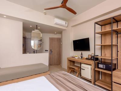 Chambre d'hôtel moderne avec lit, coin salon, TV, réfrigérateur et armoire ouverte.