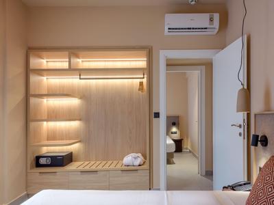Espace chambre d'hôtel moderne avec étagères en bois, climatisation et vue sur une pièce adjacente.