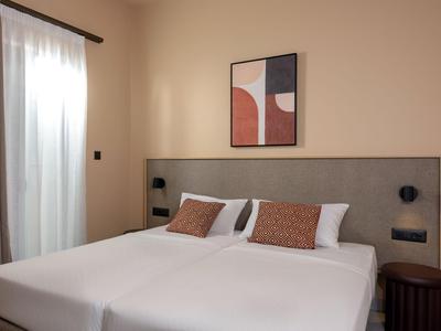 Chambre d'hôtel moderne avec deux lits simples, œuvre d'art abstraite et rideaux naturels.