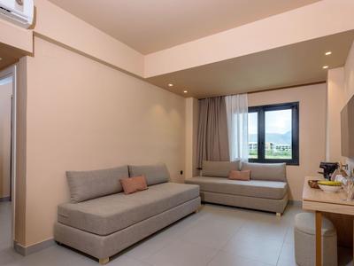 Chambre d'hôtel lumineuse avec deux canapés gris, grande fenêtre et mur décoré de façon minimaliste.