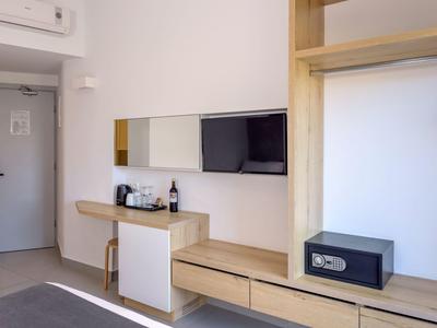Chambre d'hôtel avec mobilier en bois moderne, coffre-fort, télévision et coin café.