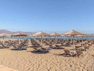 Strand mit Sand, Sonnenliegen und Sonnenschirmen, ruhiges Meer im Hintergrund.