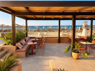 Überdachte Terrasse mit Sitzgelegenheiten bietet Meerblick und Zugang zum Strand mit Sonnenschirmen.