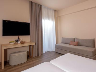 Schlicht eingerichtetes Hotelzimmer mit Doppelbett, Sofa, Schreibtisch und Fernseher an der Wand.