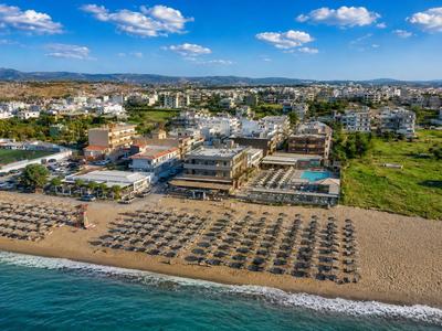 Luftaufnahme eines Hotels am Strand mit Reihen von Sonnenschirmen und blauem Himmel.