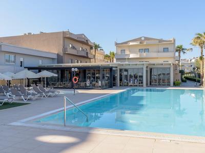 Moderner Poolbereich vor einem Hotel mit Sonnenliegen und Palmen bei klarem Himmel.