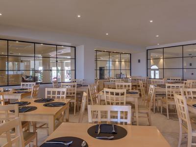 Großer, heller Speisesaal mit Holztischen und Stühlen, bestückt mit schwarzen Platzmatten.