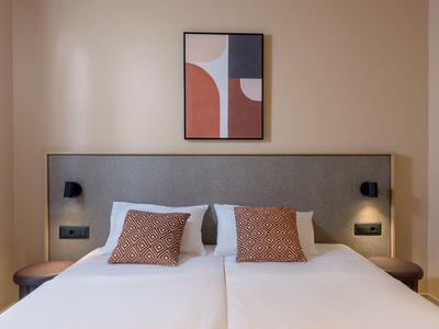 Ein modernes Hotelzimmer mit zwei Einzelbetten, grauem Kopfteil und abstraktem Wandbild.