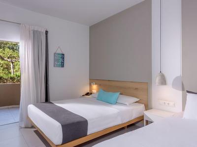 Helle Hotelzimmer mit Doppelbett, kleinen Nachttischlampen und Balkon mit Blick ins Grüne.