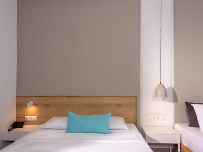 Schlichtes Hotelzimmer mit Holzkopfteil und weißer Bettwäsche, dekoriert mit türkisfarbener Kissen.