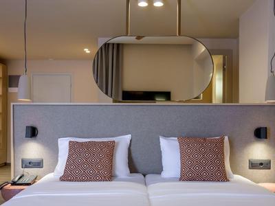 Modernes Hotelzimmer mit zwei Betten, braunen Kissen und ovalem Spiegel an der Wand.