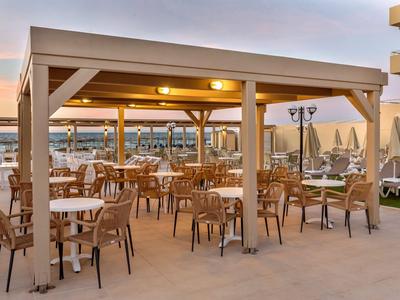 Überdachte Terrasse mit Holzstühlen und Tischen am Strand mit Sonnenliegen.