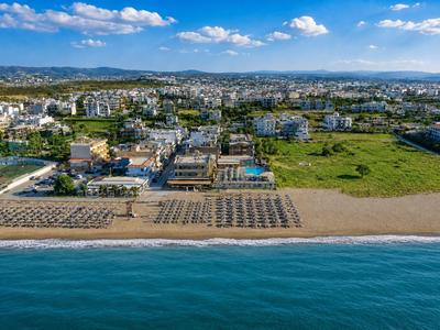 Luftaufnahme eines Strandes mit Liegestühlen vor einer Küstenstadt unter blauem Himmel.