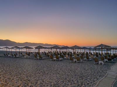 Sonnenuntergang am Strand mit Reihen von Liegestühlen und Sonnenschirmen neben ruhigem Meer.