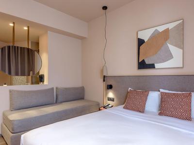 Modernes Hotelzimmer mit großem Bett, Sofa, abstraktem Bild und Hängelampe.