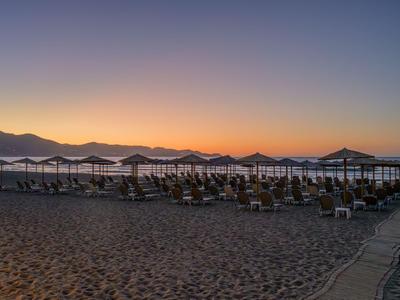 Leerer Sandstrand mit Sonnenschirmen und Stühlen bei Sonnenuntergang am Meer.
